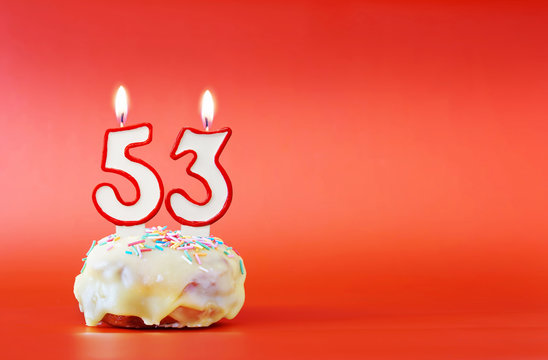Fifty three years birthday. Cupcake with white burning candle in the form of number 53. Vivid red background with copy space