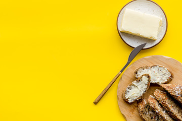 Traditional breakfast. Wholegrain bread on cutting board with butter on plate on yellow background top view copy space