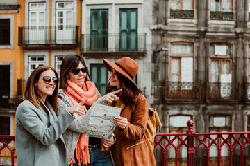 .Three beautiful and funny women traveling together in Porto, Portugal. Standing together carefree and relaxed using their map to locate themselves. Lifestyle. Travel photography