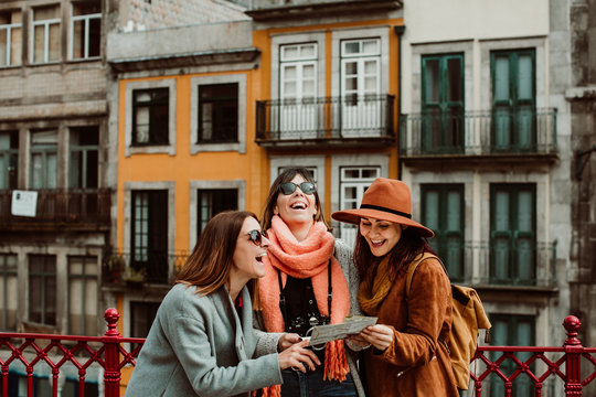 .Three beautiful and funny women traveling together in Porto, Portugal. Standing together carefree and relaxed using their map to locate themselves. Lifestyle. Travel photography