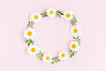 Round frame, wreath made of chamomiles, petals, leaves on beige background. Flat lay, top view