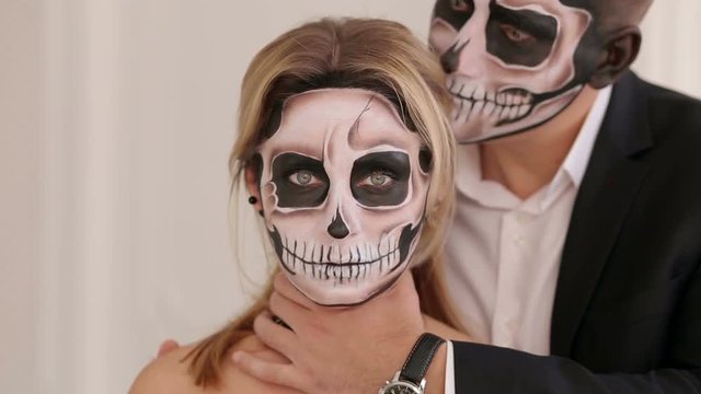 A man with a terrible make-up in the form of a zombie he hugs the girl, he puts his hand on her neck and tries to strangle her. Couple in vampire costumes in Studio. Halloween or horror concept.
