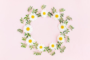 Round frame, wreath made of chamomiles, petals, leaves on beige background. Flat lay, top view
