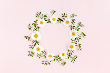 Round frame, wreath made of chamomiles, petals, leaves on beige background. Flat lay, top view