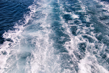 Turbulence made by foam of sea water from a high-speed yacht on surface of sea. Blue sea waves with lot of sea foam. Surface of sea with waves, splash, foam and bubbles, blue background and wallpaper.