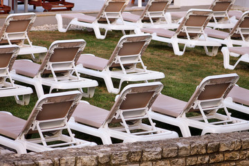 Exotic beach on mediterranean sea, sunbeds for sunbathing and relax on grass in tropical garden of luxury resort hotel. Sun loungers on lawn waiting for tourists. Idyllic seaside in summer season.