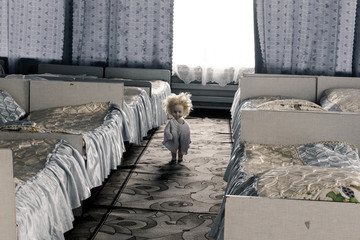 Creepy doll with yellow hair stands between the beds