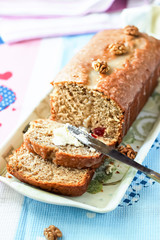 Banana bread or cake healthy and tasty breakfast. Loaf with walnuts, icing and cream cheese. Pink and blue towel background. Selective focus.