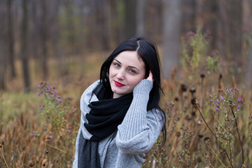 Horizontal portrait of pretty brunette young woman with porcelain skin and red lips touching her hair and standing in front of soft focus Fall foliage