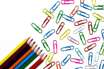 Many multi-colored stationery clips for documents and multi-colored pencils lie on a white background