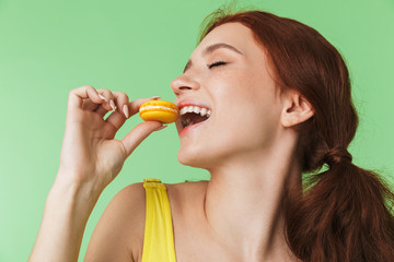 Redhead girl posing isolated over green wall background holding sweeties macaroons.