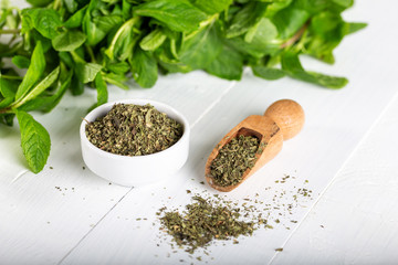 Dried peppermint in a white bowl and a bunch of fresh mint, on wooden background. Food background.