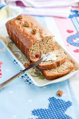 Banana bread or cake healthy and tasty breakfast. Loaf with walnuts, icing and cream cheese. Pink and blue towel background. Selective focus.