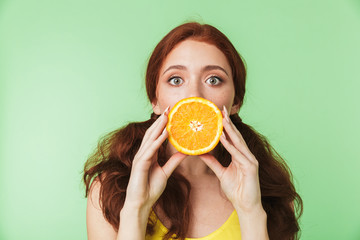 Young redhead girl posing isolated over green wall background with citrus vitamins fruits.