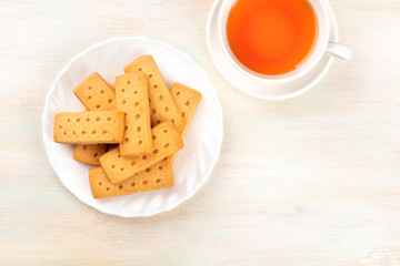 A closeup photo of Scottish shortbread butter cookies, shot from above on a white wooden background with a cup of tea and a place for text