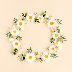 Wreath made of chamomiles, petals, leaves on beige background. Flat lay, top view floral background.