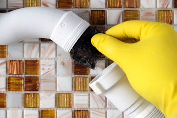 Elimination of blockage in sewer pipes. Hands in yellow gloves disassemble and clean the sink...
