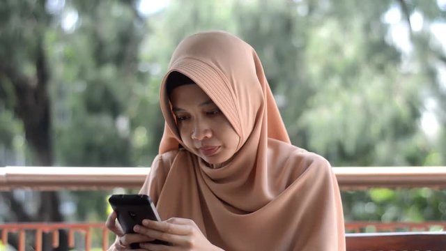 Muslim south east asian woman with hijab is using her smartphone to make a call