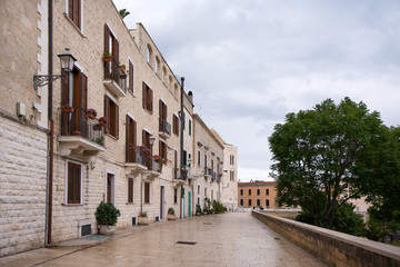 Fototapeta na wymiar Romantic and historical paved, polished stone sidewalk in Bari, Italy on overcast summer day. White buildings in old town with flower decorations in front of apartments and houses. Concept of travel