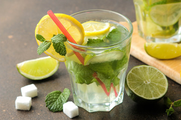 Mojito cocktail in a glass tumbler with lime, mint and lemon and on a dark concrete background. make a mojito.