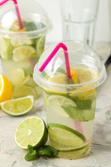 Mojito cocktail in a plastic glass with lime, mint and lemon on a light concrete table. make a mojito.