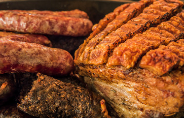 Roasted crispy pork ribs ,black pudding and sausages in oval metal baking dish.