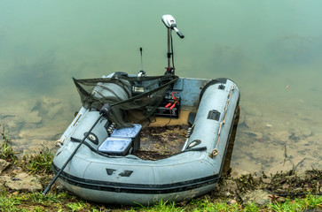 Fishing tackle rubber boat with electric motor parked at river bank.