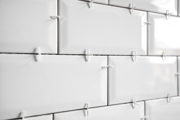 Ceramic tile lying. Installing new subway or metro tiles in bathroom, shower or kitchen back splash during home renovation. Placing or taking out tile spacers with hands and pliers.