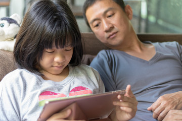 Father and daughter concept. Daddy working on computer notebook hand typing on keyboard while Asia kid girl using tablet hand touching on touchscreen playing game.