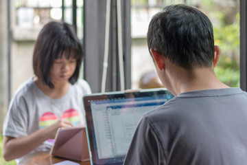 Father and daughter concept. Daddy working on computer notebook hand typing on keyboard while Asia kid girl using tablet hand touching on touchscreen playing game.