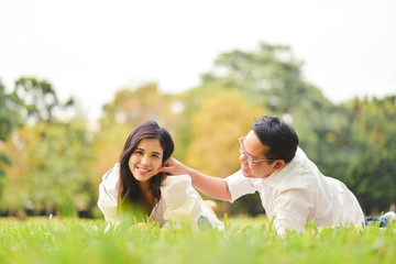 Portrait of happy  young asian couple laying on grass In public park.