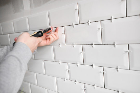 Ceramic tile lying. Installing new subway or metro tiles in bathroom, shower or kitchen back splash during home renovation. Placing or taking out tile spacers with hands and pliers.
