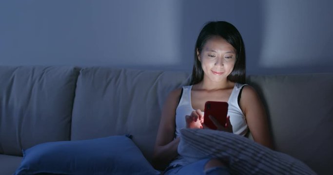 Woman use of smart phone and sit on sofa at home in the evening