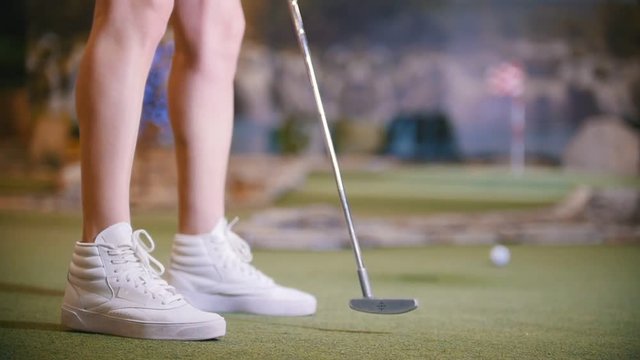 A young woman playing mini golf indoors. Legs in the frame