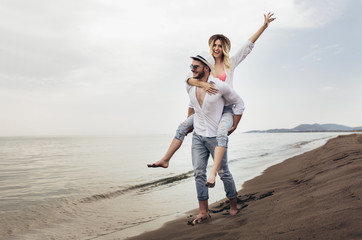 Happy couple in love on beach summer vacations. Joyful girl piggybacking on young boyfriend having fun.