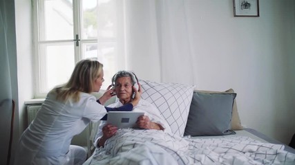 A health visitor helping a sick senior woman in bed at home.