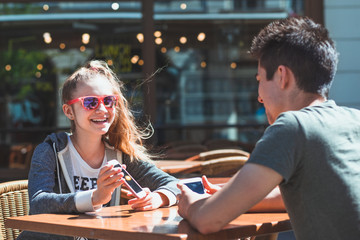 Fototapeta premium Young woman and man sitting in pavement cafe talking and using mobile phones