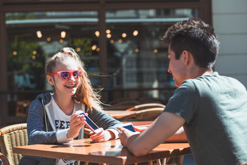 Young woman and man sitting in pavement cafe talking and using mobile phones