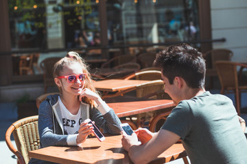 Young woman and man sitting in pavement cafe talking and using mobile phones