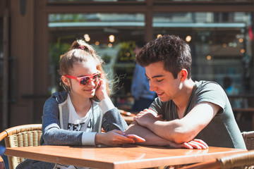 Young woman and man sitting in pavement cafe talking and using mobile phones