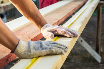 Close up view of a man hands measuring wooden plank with a tape line.