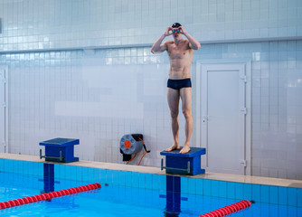 Muscular swimmer preparing to jump from starting block in a swimming pool