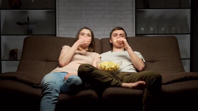 Young couple watching tv and eating popcorn at home.