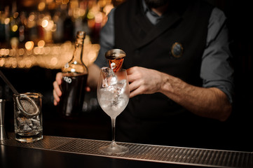 Bartender pouring a delicious cocktail from the steel jigger