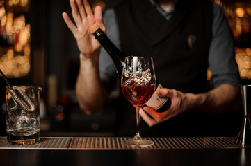 Bartender holding a bottle on the foreground of glass with a cocktail