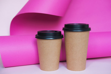 Coffee cup on pink paper background. A couple of paper cups of coffee to take away.