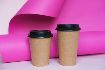 Coffee cup on pink paper background. A couple of paper cups of coffee to take away.