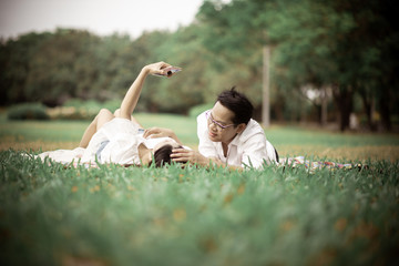 Portrait of happy  young asian couple laying on grass In public park.