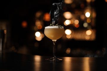 Delicious cocktail with a foam in the glass decorated with a smoked herb