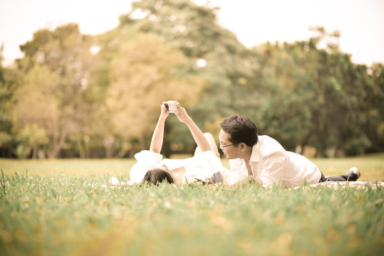 Portrait of happy  young asian couple laying on grass In public park.